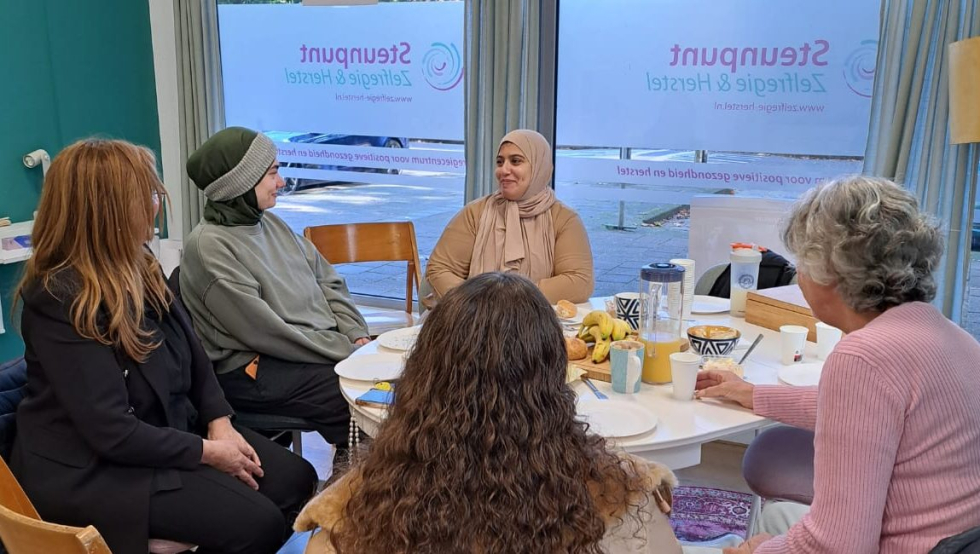 Een foto van 5 vrouwen die rond een tafel zitten tijdens de bijeenkomst