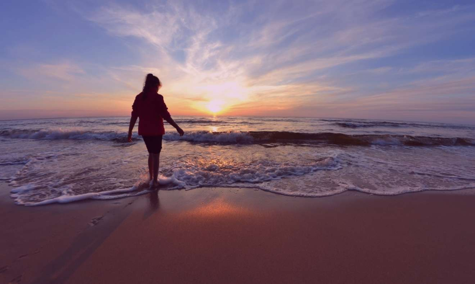 Iemand wandelt over het strand rond zonsondergang