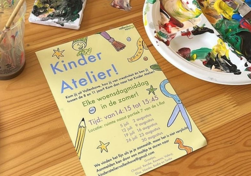 Foto van een flyer voor het Kinder Atelier op een tafel met kwasten en verf