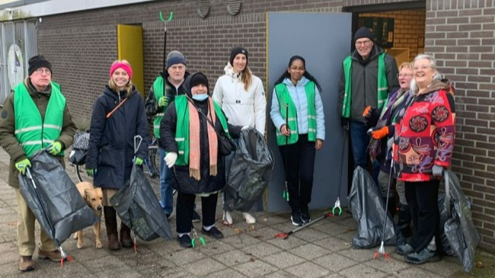 Een groep van 9 vrijwilligers met groene hesjes aan en afvalprikkers met vuilniszakken in hun handen. 